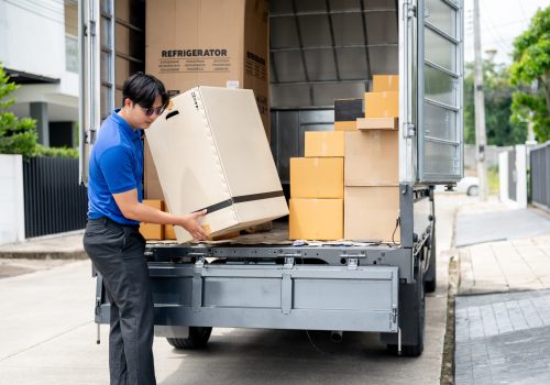 An Asian delivery man or mover in a blue uniform is unloading cardboard boxes from his truck. cargo, courier, freight, shipping service, house moving service