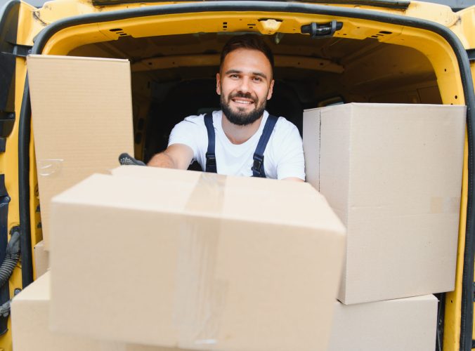 Courier smiling while holding a cardboard box inside a delivery van packed with packages, embodying the spirit of efficient logistics and service